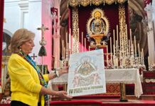 Casi treinta hermandades se citan en Vélez-Málaga con sus patronas Encuentro de Patronas en Vélez-Málaga: mujer con el cartel del encuentro ante el altar de la iglesia