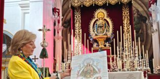 Casi treinta hermandades se citan en Vélez-Málaga con sus patronas Encuentro de Patronas en Vélez-Málaga: mujer con el cartel del encuentro ante el altar de la iglesia